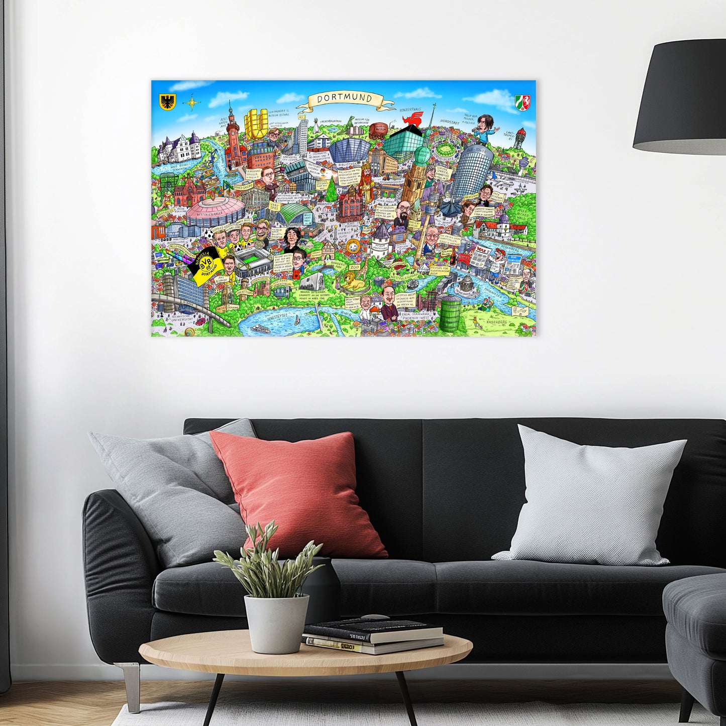 Jacques Tilly Dortmund Stadtbild auf Leinwand mit Holzrahmen über einem schwarzen Sofa mit einem roten und zwei grauen Kissen und einem runden Couchtisch aus Holz davor.