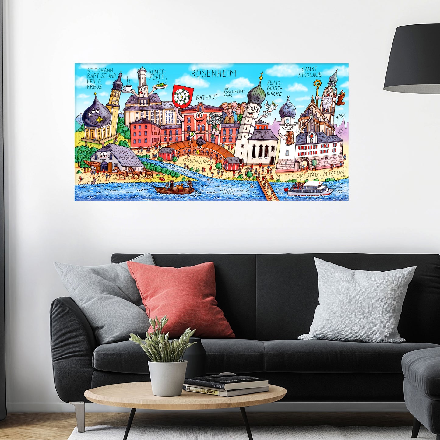 Jacques Tilly Rosenheim Stadtbild auf Leinwand mit Holzrahmen über einem schwarzen Sofa mit einem roten und zwei grauen Kissen und einem runden Couchtisch aus Holz davor.
