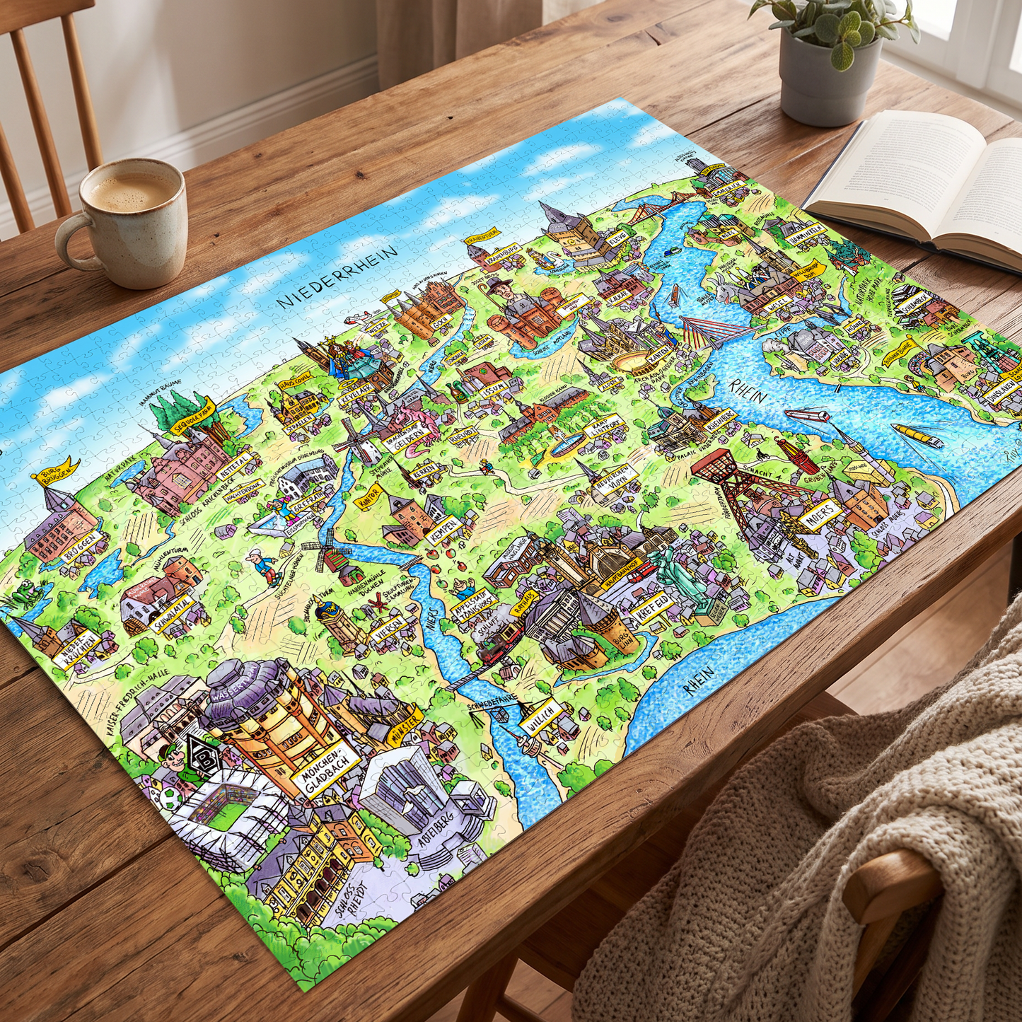 Gelegtes Niederrhein Puzzle auf einem Holztisch neben einer Kaffeetasse und einem Buch.