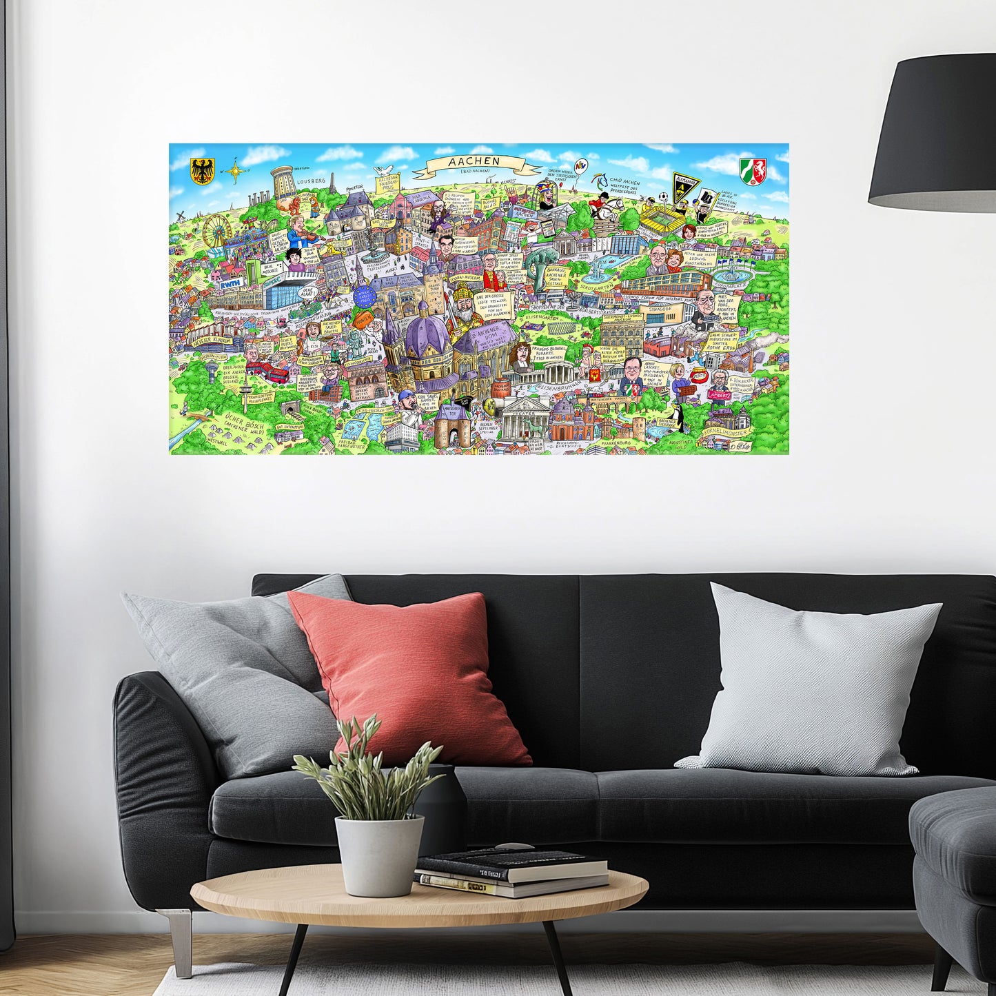 Jacques Tilly Aachen Stadtbild als Acrylbild mit Alu-Rückrahmen über einem schwarzen Sofa mit einem roten und zwei grauen Kissen und einem runden Couchtisch aus Holz davor.