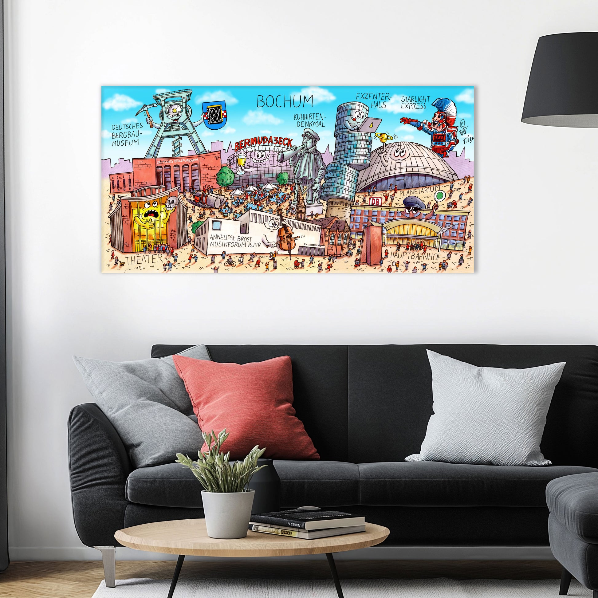 Jacques Tilly Bochum Stadtbild als Acrylbild mit Alu-Rückrahmen über einem schwarzen Sofa mit einem roten und zwei grauen Kissen und einem runden Couchtisch aus Holz davor.
