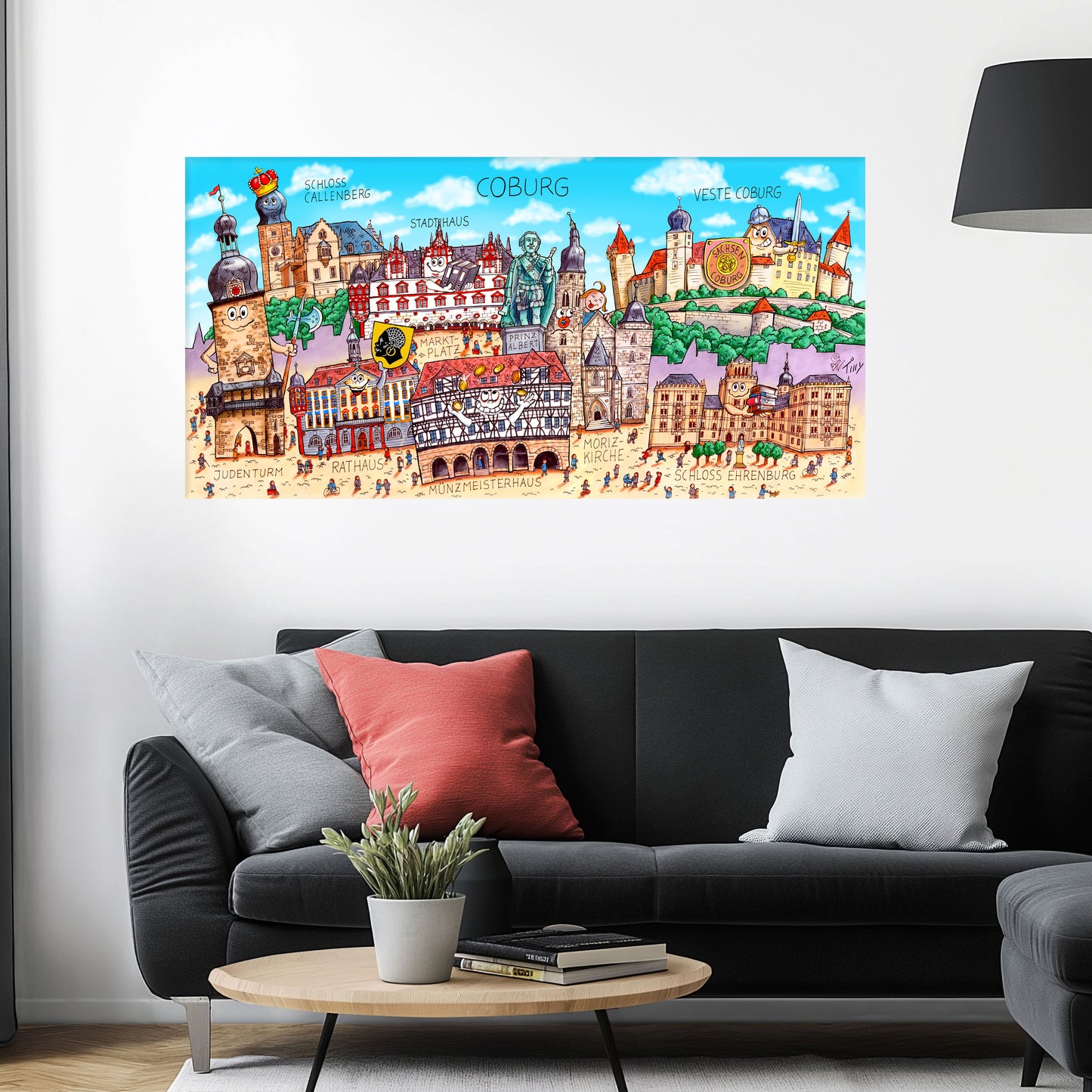 Jacques Tilly Coburg Stadtbild als Acrylbild mit Alu-Rückrahmen über einem schwarzen Sofa mit einem roten und zwei grauen Kissen und einem runden Couchtisch aus Holz davor.