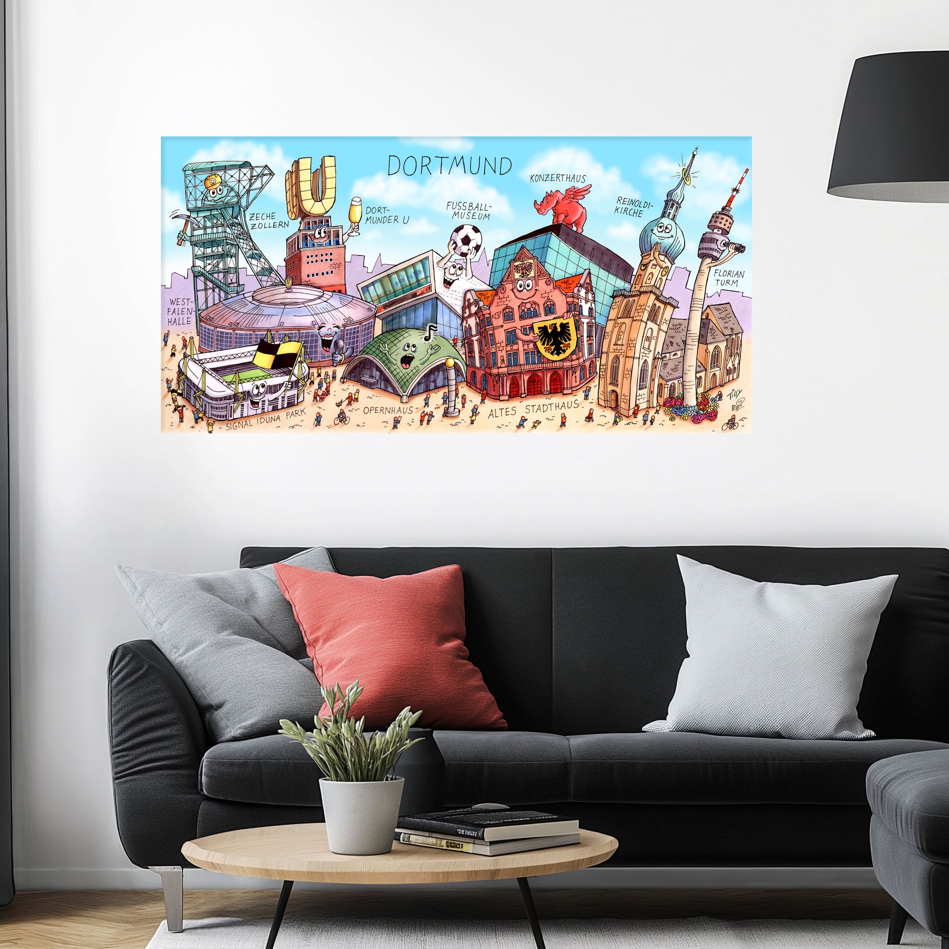 Jacques Tilly Dortmund Stadtbild als Acrylbild mit Alu-Rückrahmen über einem schwarzen Sofa mit einem roten und zwei grauen Kissen und einem runden Couchtisch aus Holz davor.