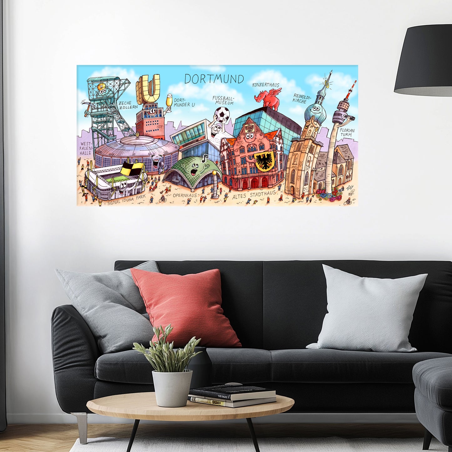 Jacques Tilly Dortmund Stadtbild auf Leinwand mit Holzrahmen über einem schwarzen Sofa mit einem roten und zwei grauen Kissen und einem runden Couchtisch aus Holz davor.