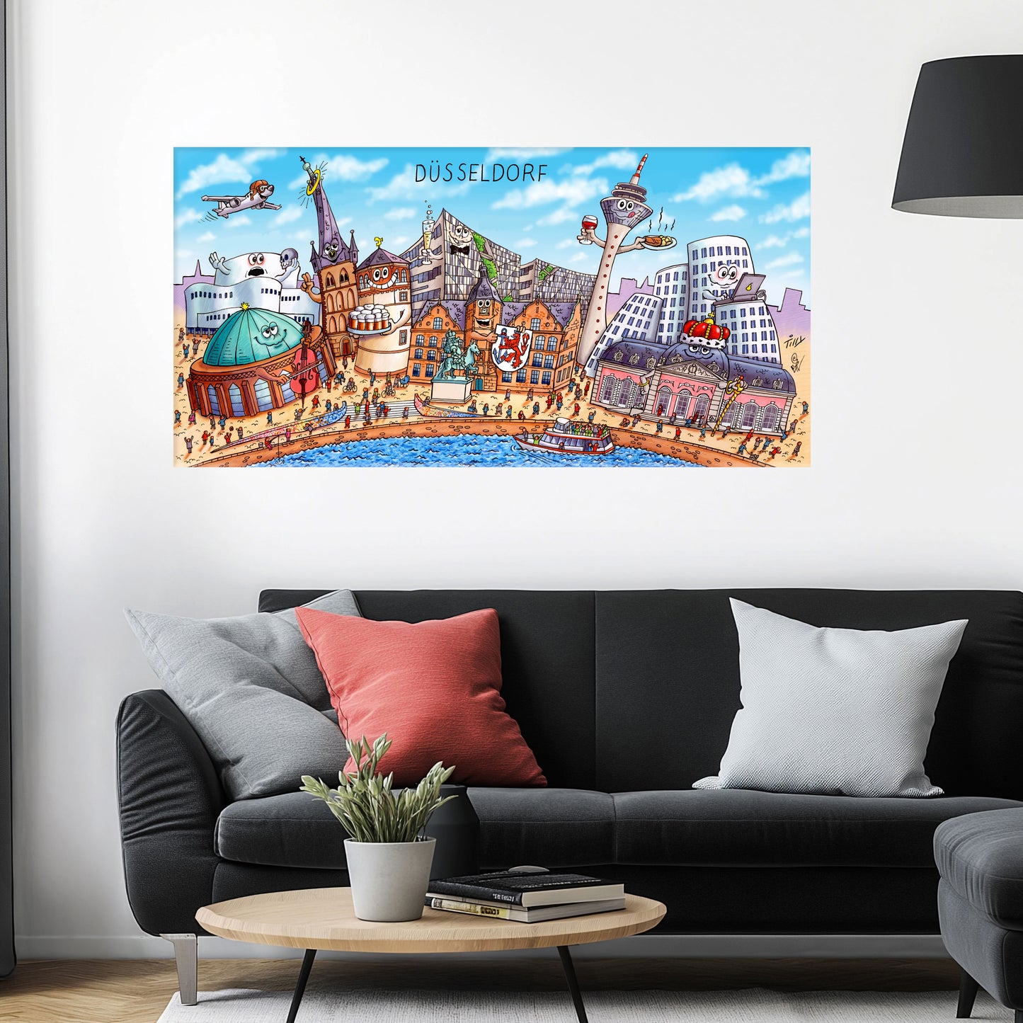 Jacques Tilly Düsseldorf Stadtbild als Acrylbild mit Alu-Rückrahmen über einem schwarzen Sofa mit einem roten und zwei grauen Kissen und einem runden Couchtisch aus Holz davor.