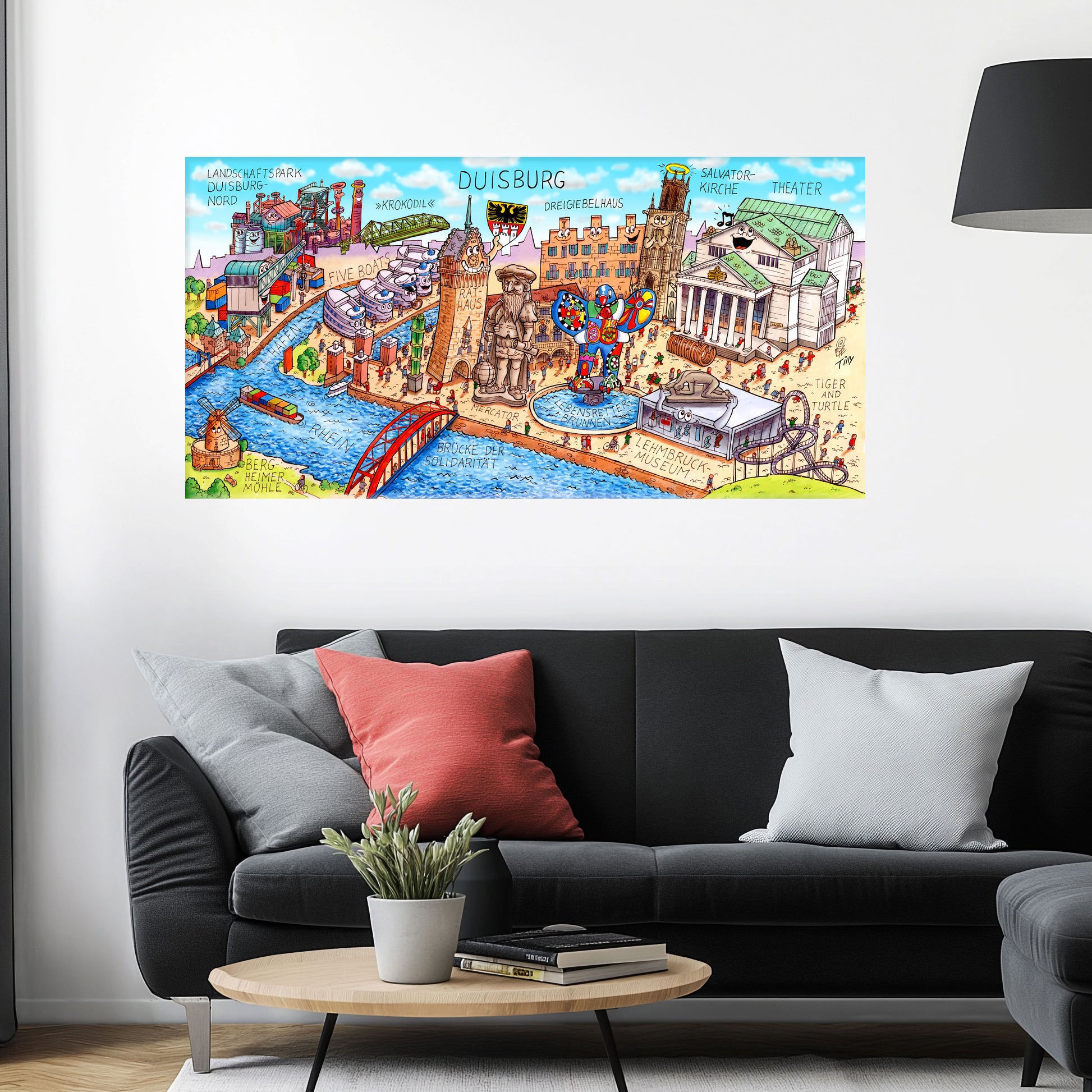 Jacques Tilly Duisburg Stadtbild als Acrylbild mit Alu-Rückrahmen über einem schwarzen Sofa mit einem roten und zwei grauen Kissen und einem runden Couchtisch aus Holz davor.