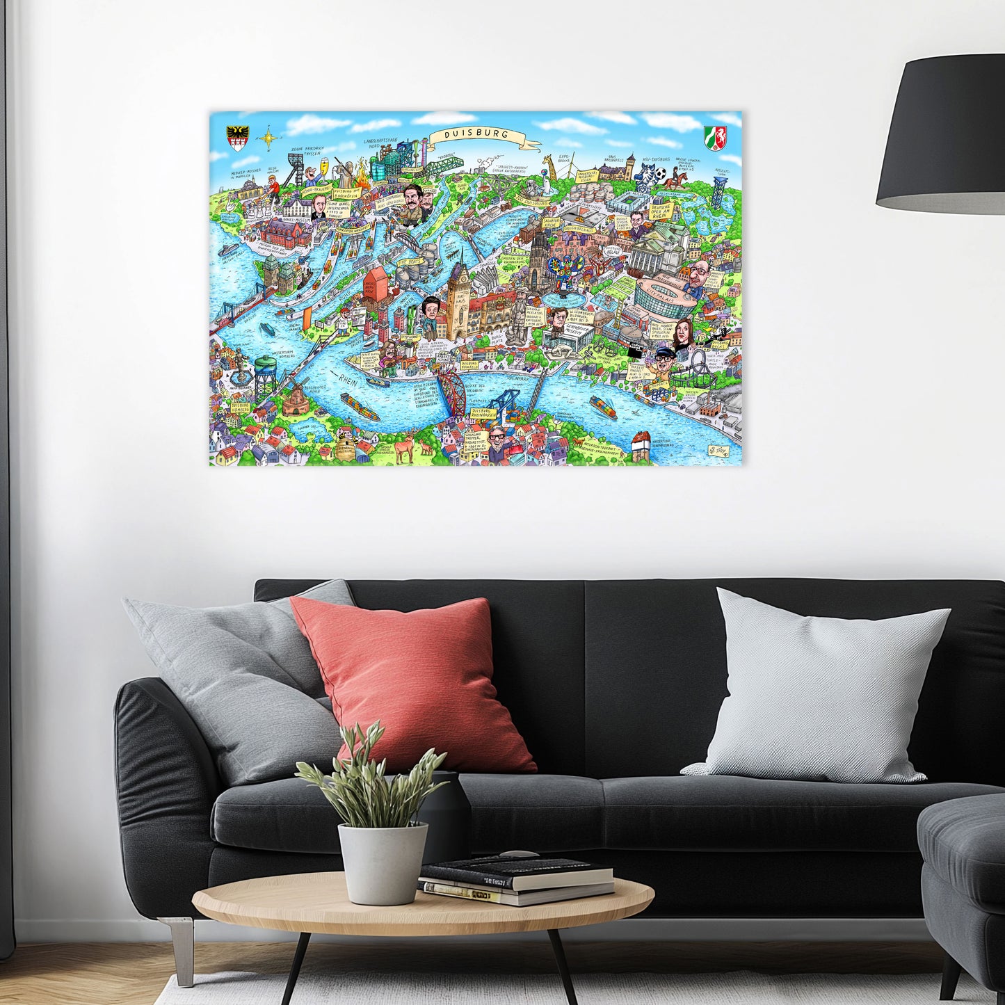 Jacques Tilly Duisburg Stadtbild als Acrylbild mit Alu-Rückrahmen über einem schwarzen Sofa mit einem roten und zwei grauen Kissen und einem runden Couchtisch aus Holz davor.