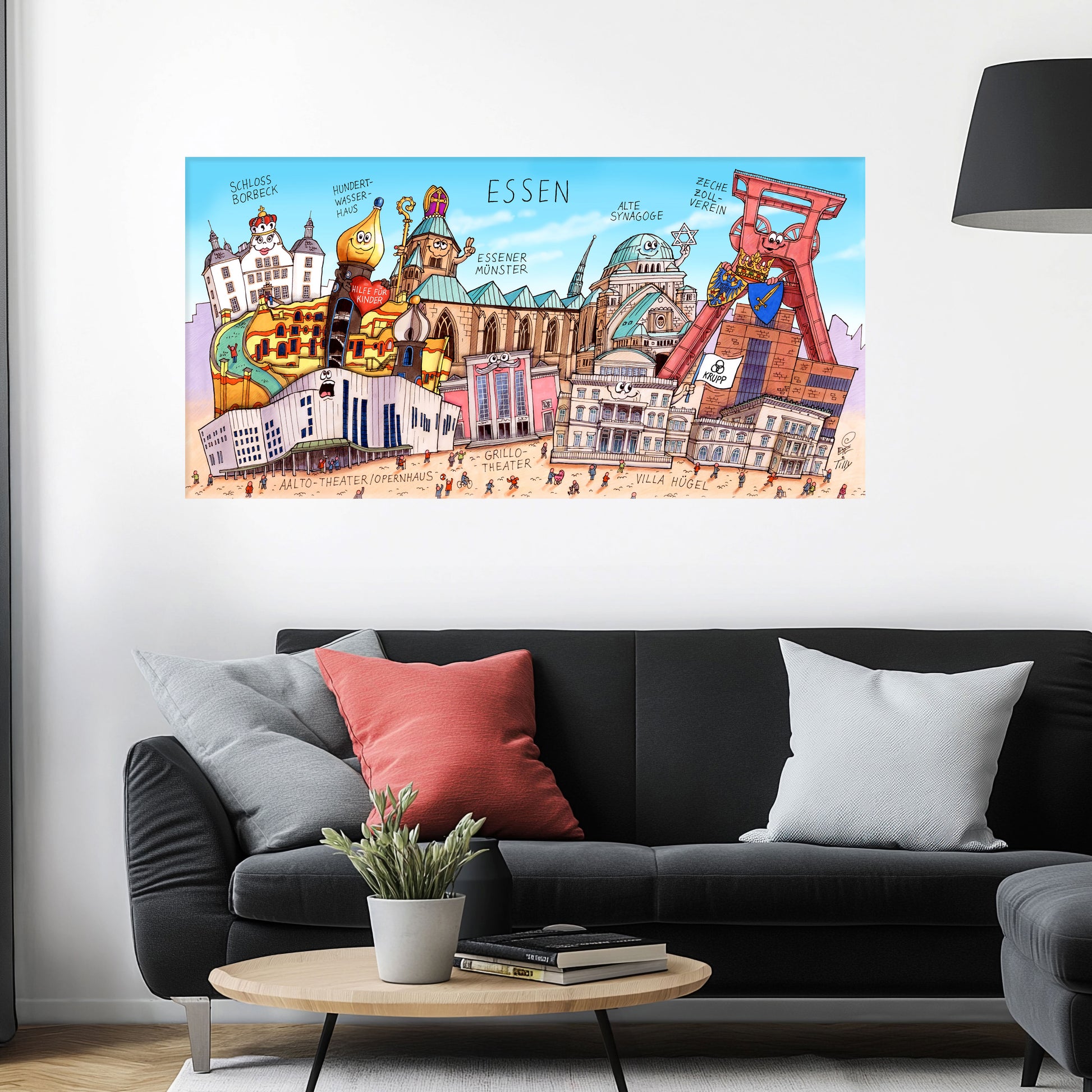 Jacques Tilly Essen Stadtbild auf Leinwand mit Holzrahmen über einem schwarzen Sofa mit einem roten und zwei grauen Kissen und einem runden Couchtisch aus Holz davor.