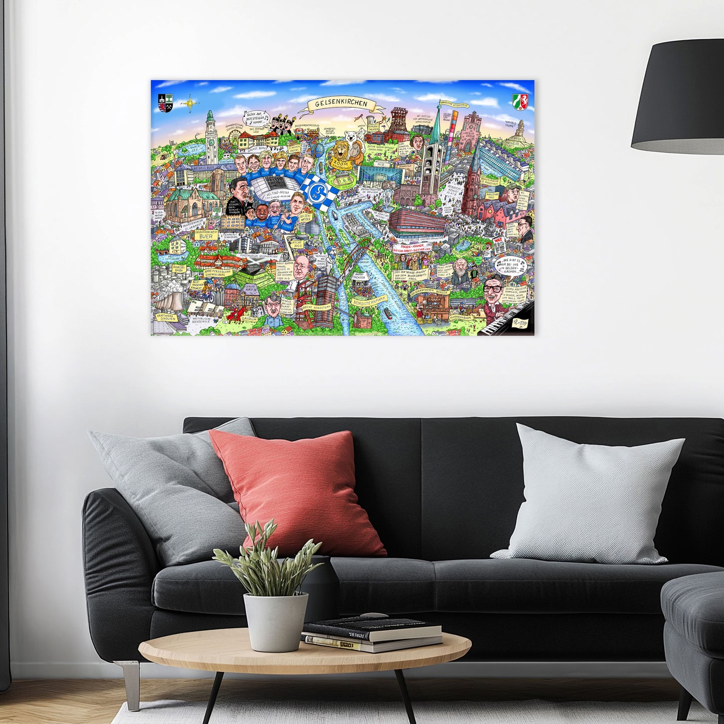 Jacques Tilly Gelsenkirchen Stadtbild auf Leinwand mit Holzrahmen über einem schwarzen Sofa mit einem roten und zwei grauen Kissen und einem runden Couchtisch aus Holz davor.