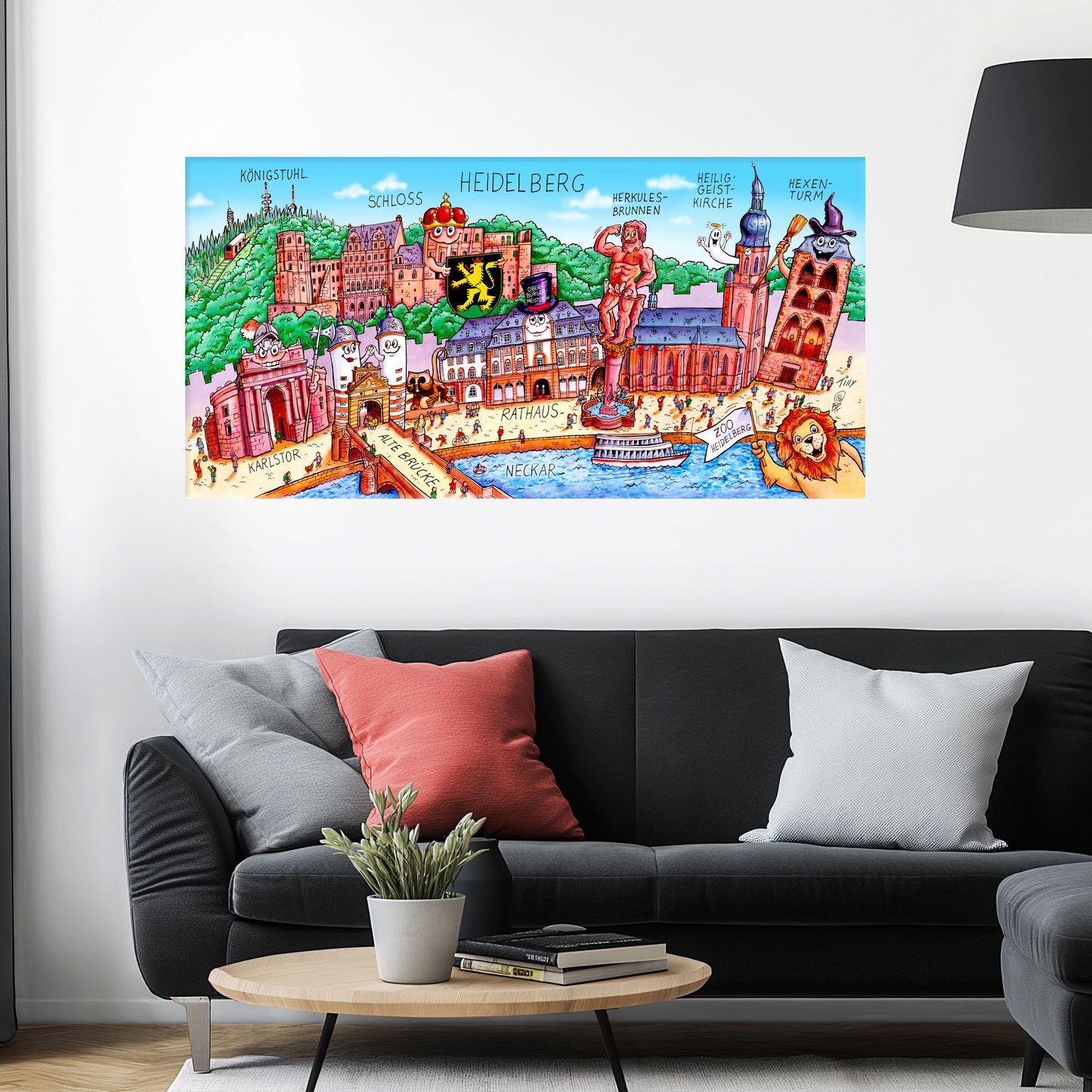 Jacques Tilly Heidelberg Stadtbild auf Leinwand mit Holzrahmen über einem schwarzen Sofa mit einem roten und zwei grauen Kissen und einem runden Couchtisch aus Holz davor.