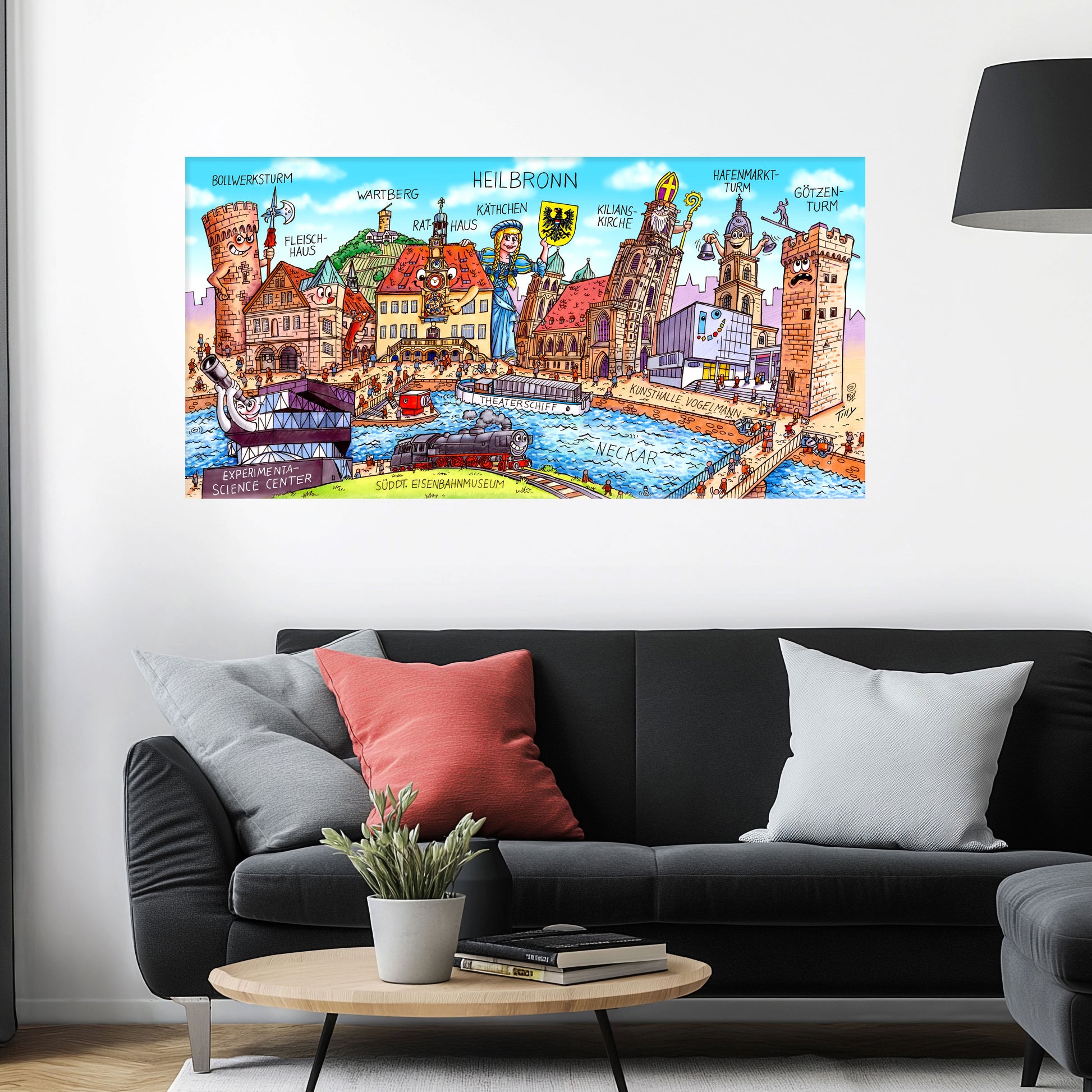 Jacques Tilly Heilbronn Stadtbild auf Leinwand mit Holzrahmen über einem schwarzen Sofa mit einem roten und zwei grauen Kissen und einem runden Couchtisch aus Holz davor.