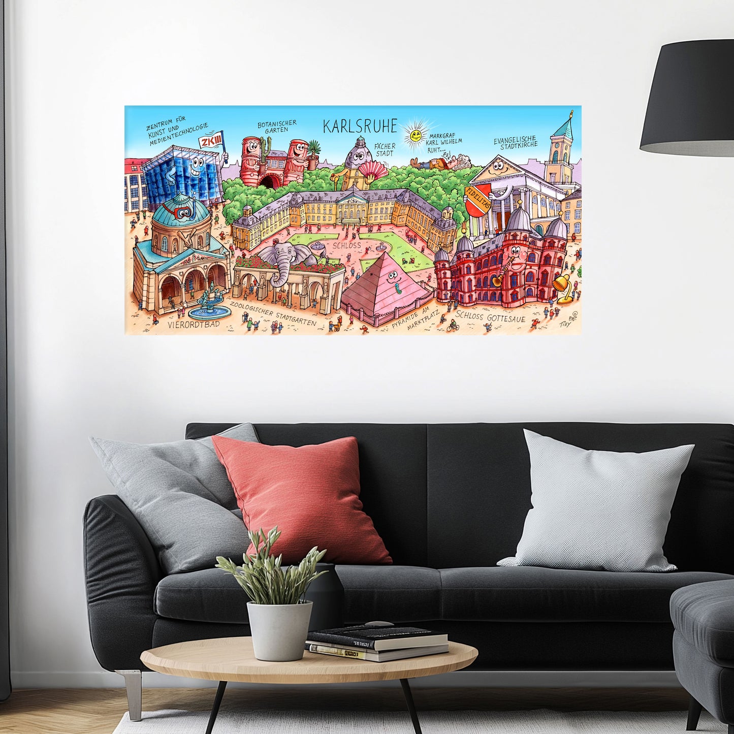 Jacques Tilly Karlsruhe Stadtbild auf Leinwand mit Holzrahmen über einem schwarzen Sofa mit einem roten und zwei grauen Kissen und einem runden Couchtisch aus Holz davor.