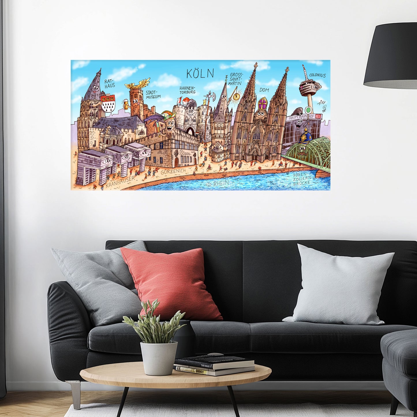 Jacques Tilly Köln Stadtbild auf Leinwand mit Holzrahmen über einem schwarzen Sofa mit einem roten und zwei grauen Kissen und einem runden Couchtisch aus Holz davor.