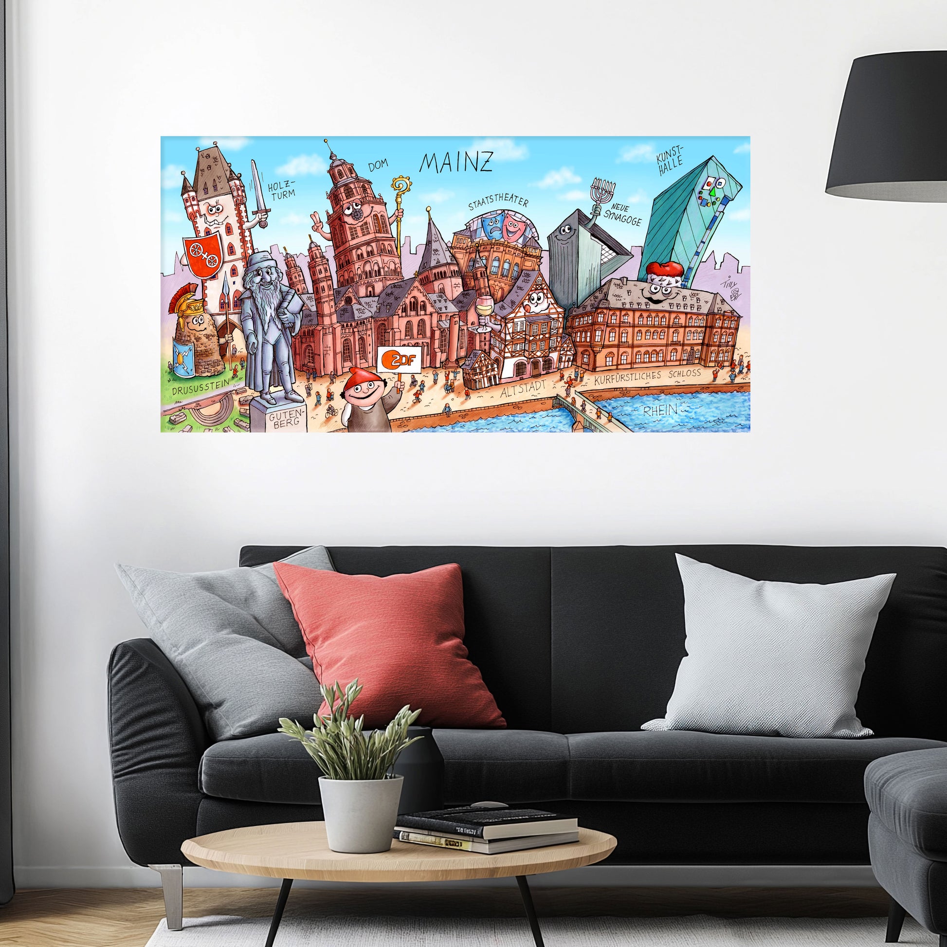 Jacques Tilly Mainz Stadtbild als Acrylbild mit Alu-Rückrahmen über einem schwarzen Sofa mit einem roten und zwei grauen Kissen und einem runden Couchtisch aus Holz davor.