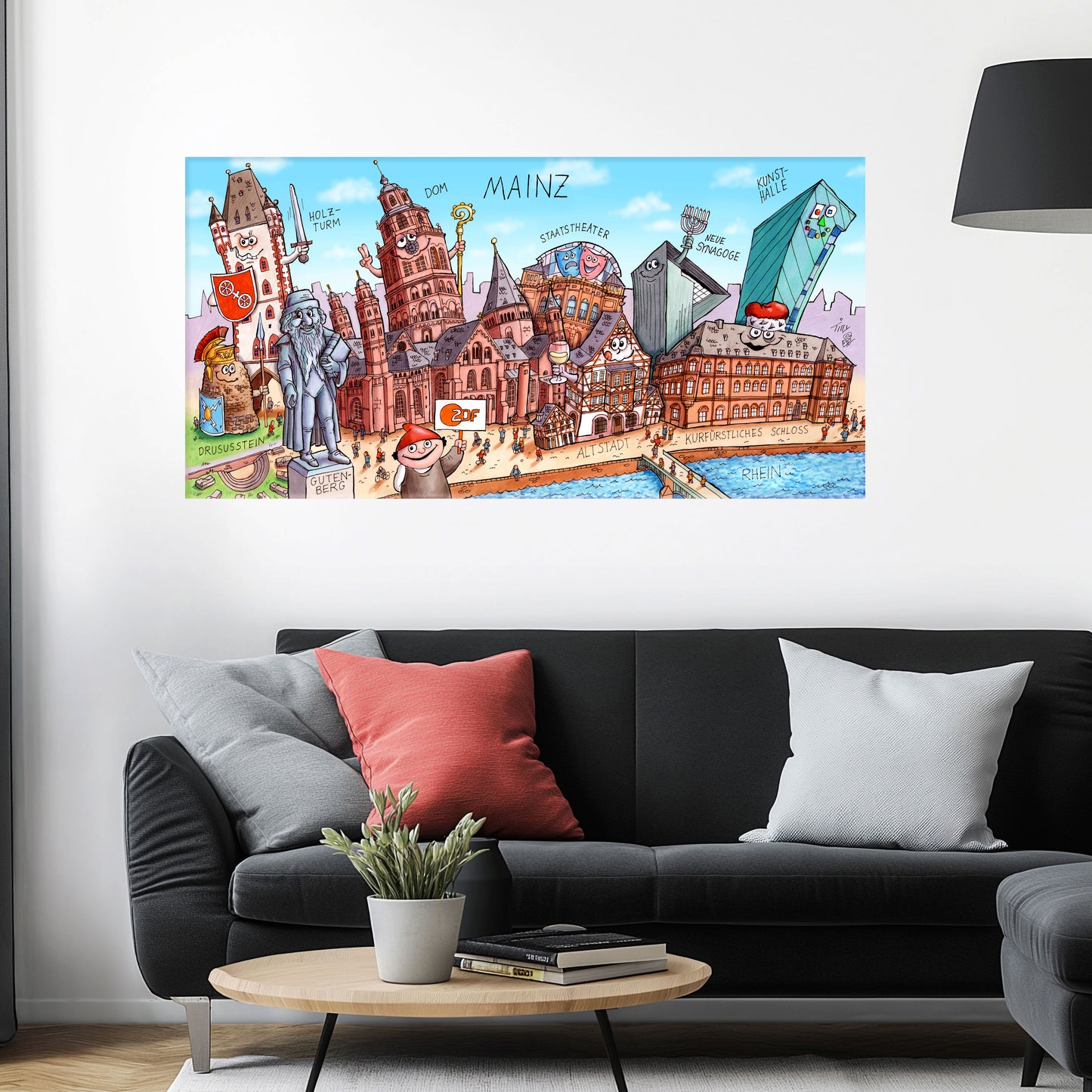 Jacques Tilly Mainz Stadtbild auf Leinwand mit Holzrahmen über einem schwarzen Sofa mit einem roten und zwei grauen Kissen und einem runden Couchtisch aus Holz davor.