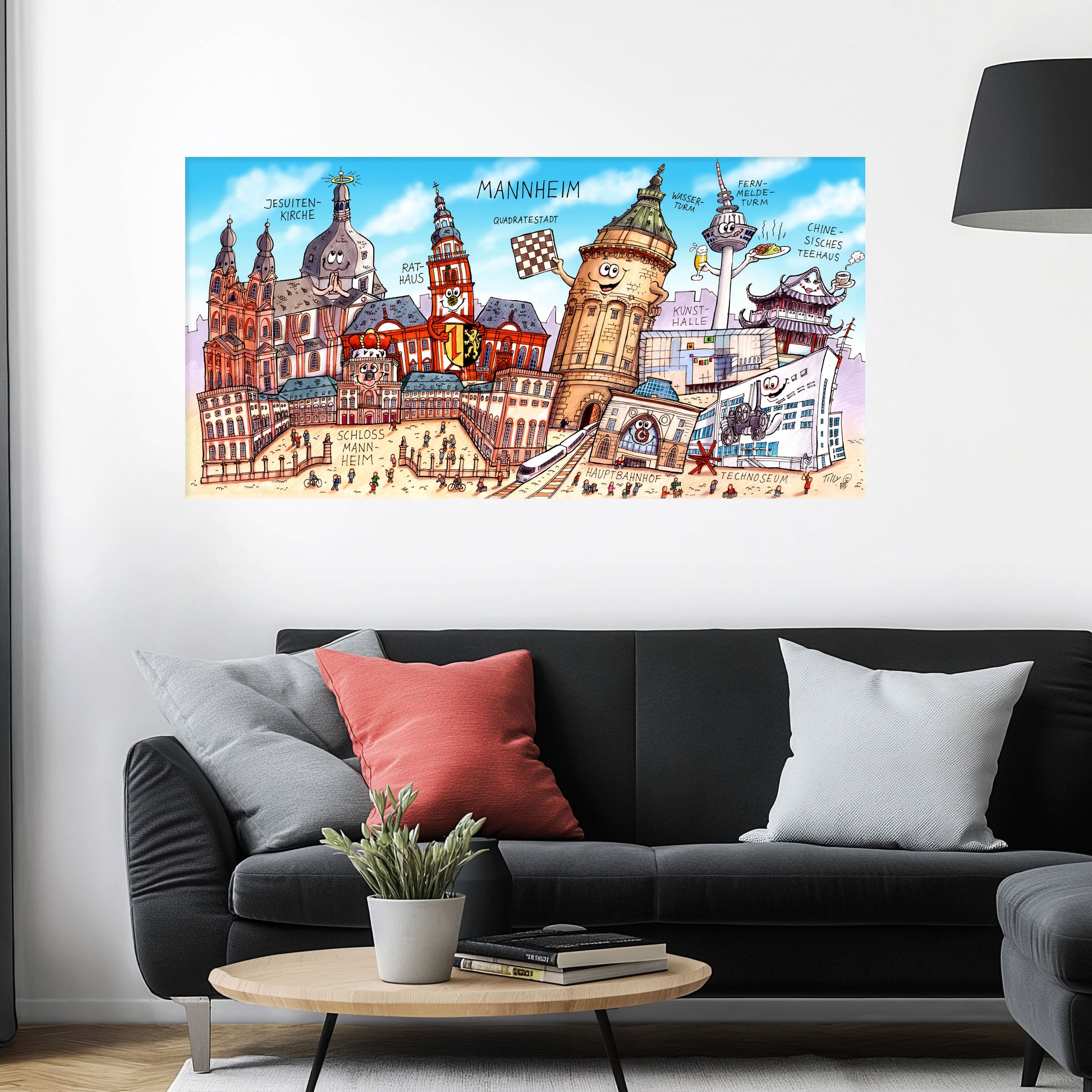 Jacques Tilly Mannheim Stadtbild als Acrylbild mit Alu-Rückrahmen über einem schwarzen Sofa mit einem roten und zwei grauen Kissen und einem runden Couchtisch aus Holz davor.
