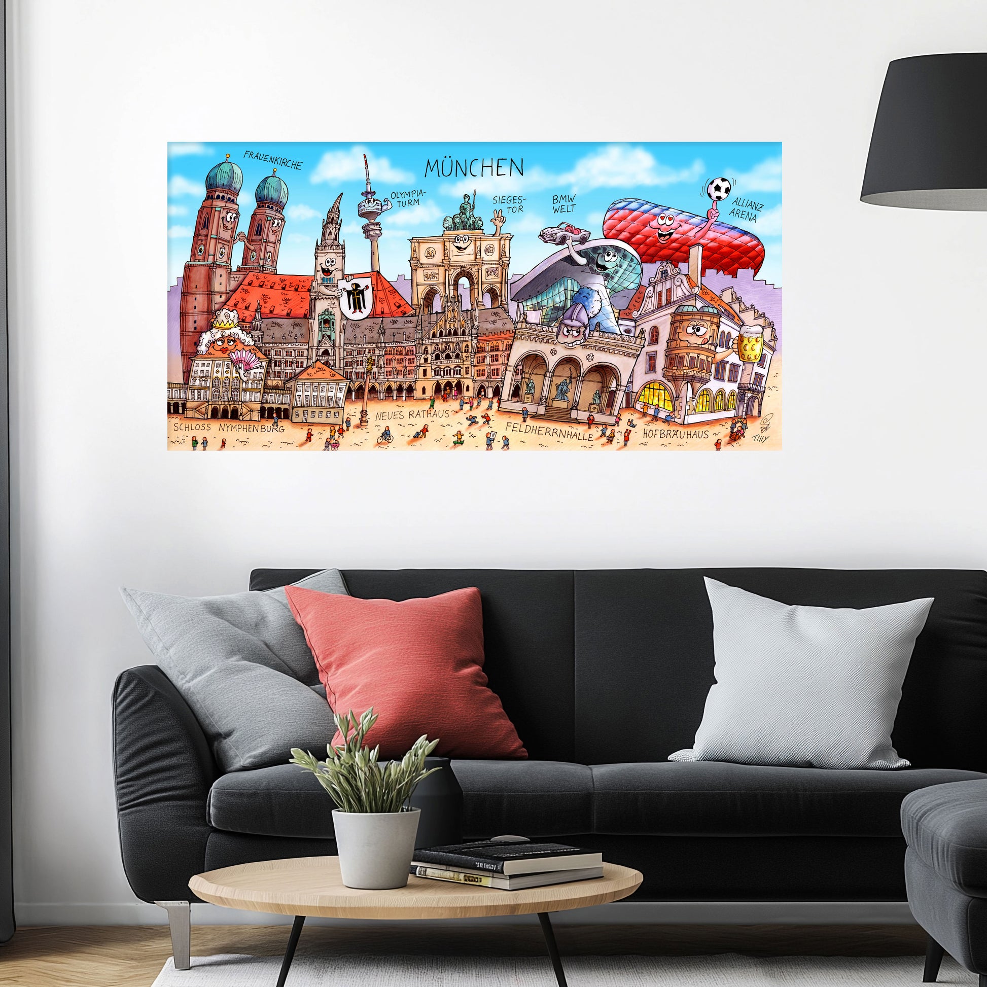 Jacques Tilly München Stadtbild auf Leinwand mit Holzrahmen über einem schwarzen Sofa mit einem roten und zwei grauen Kissen und einem runden Couchtisch aus Holz davor.