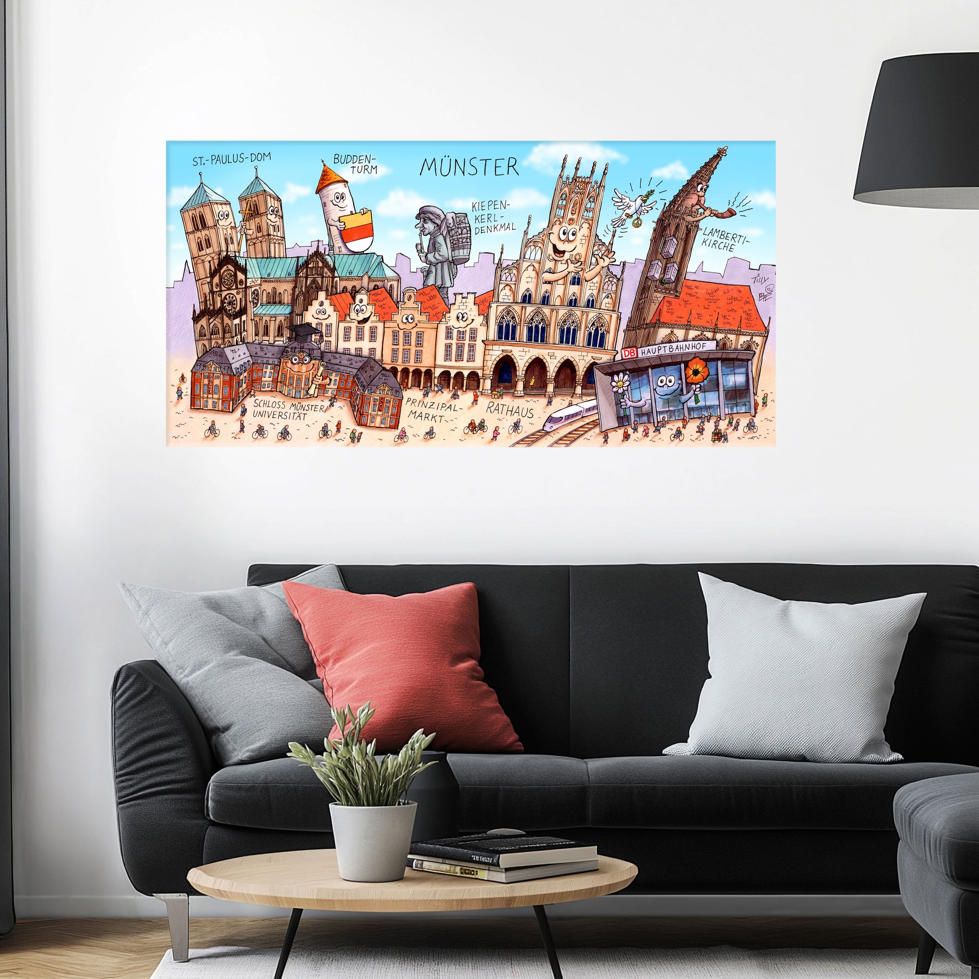 Jacques Tilly Münster Stadtbild als Acrylbild mit Alu-Rückrahmen über einem schwarzen Sofa mit einem roten und zwei grauen Kissen und einem runden Couchtisch aus Holz davor.