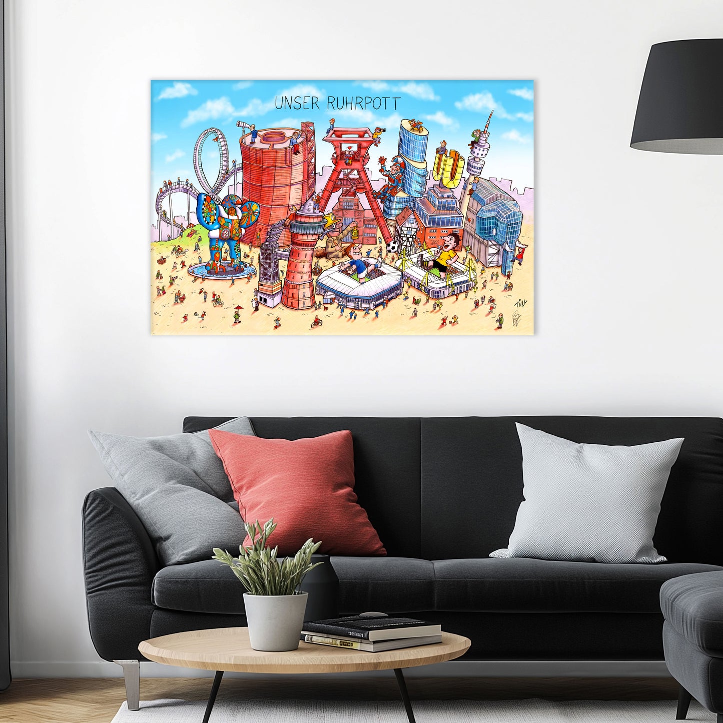 Jacques Tilly Ruhrpott Wimmelbild auf Leinwand mit Holzrahmen über einem schwarzen Sofa mit einem roten und zwei grauen Kissen und einem runden Couchtisch aus Holz davor.