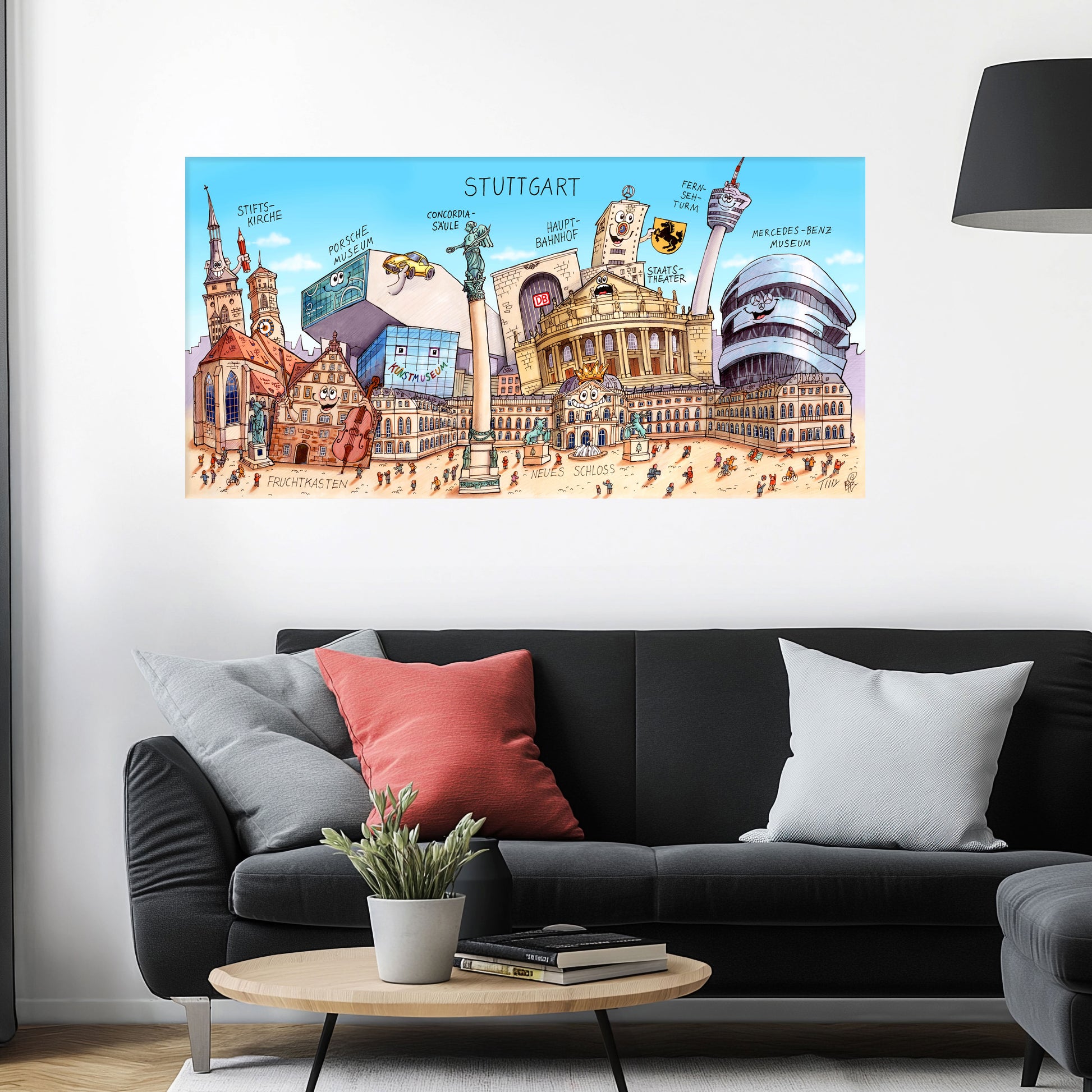 Jacques Tilly Stuttgart Stadtbild auf Leinwand mit Holzrahmen über einem schwarzen Sofa mit einem roten und zwei grauen Kissen und einem runden Couchtisch aus Holz davor.