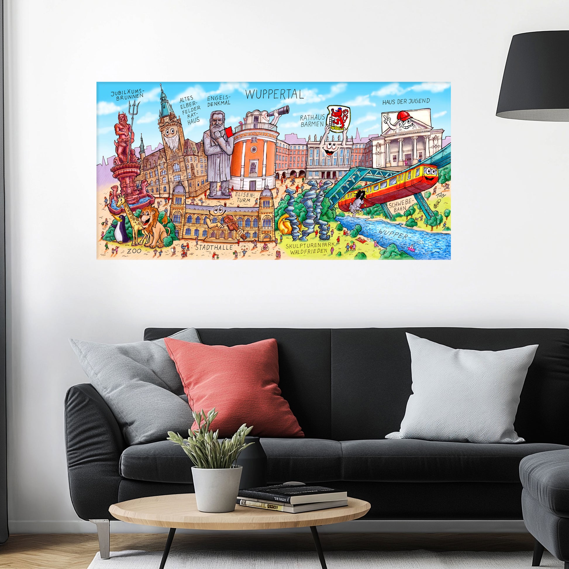 Jacques Tilly Wuppertal Stadtbild als Acrylbild mit Alu-Rückrahmen über einem schwarzen Sofa mit einem roten und zwei grauen Kissen und einem runden Couchtisch aus Holz davor.